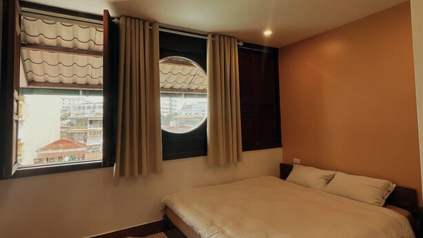 Quarto com uma cama de solteiro, janela com cortinas e vista para edifícios.