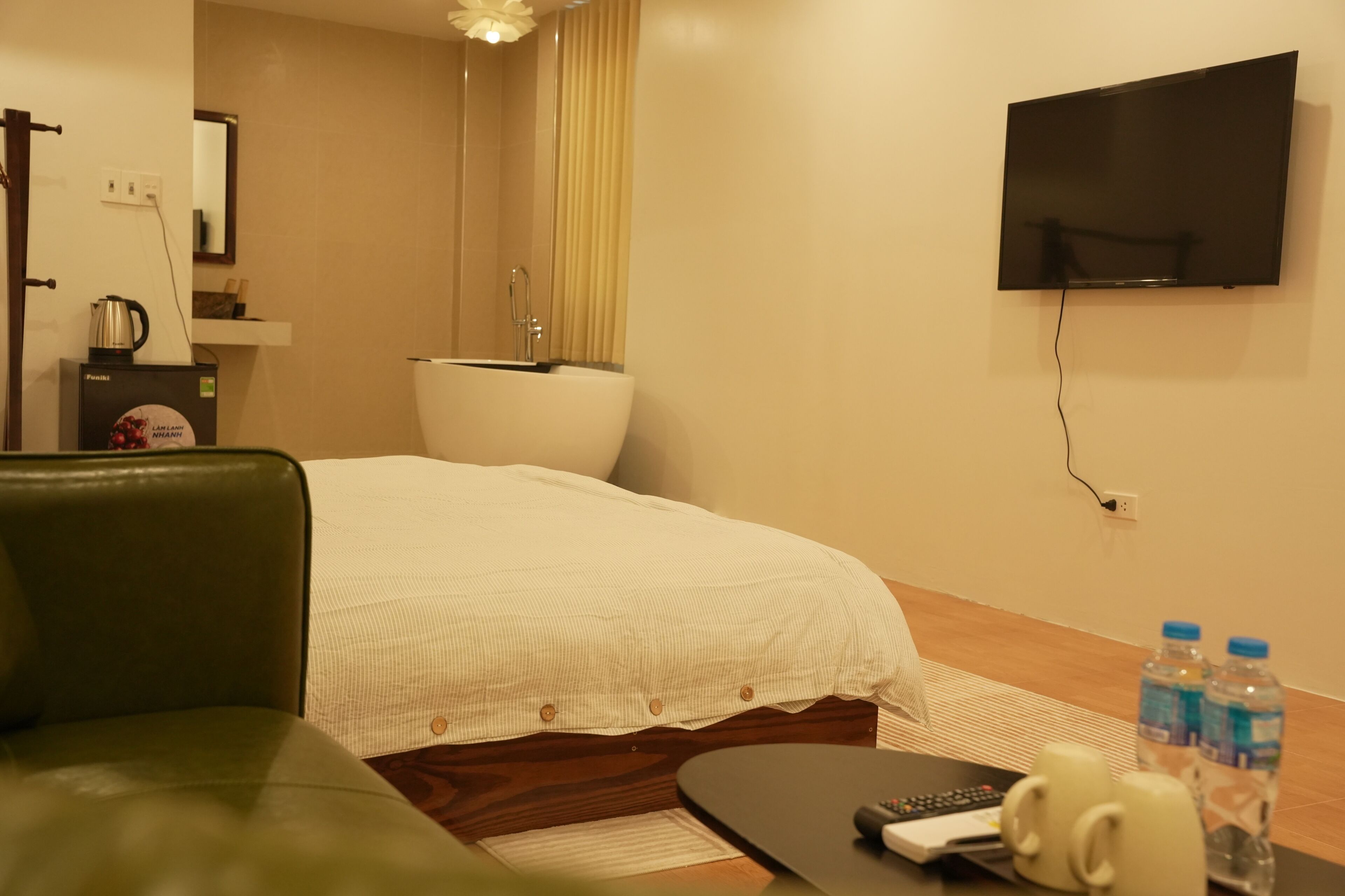 A hotel room with a bed, a green sofa, a television mounted on the wall, and a coffee maker on the side table.