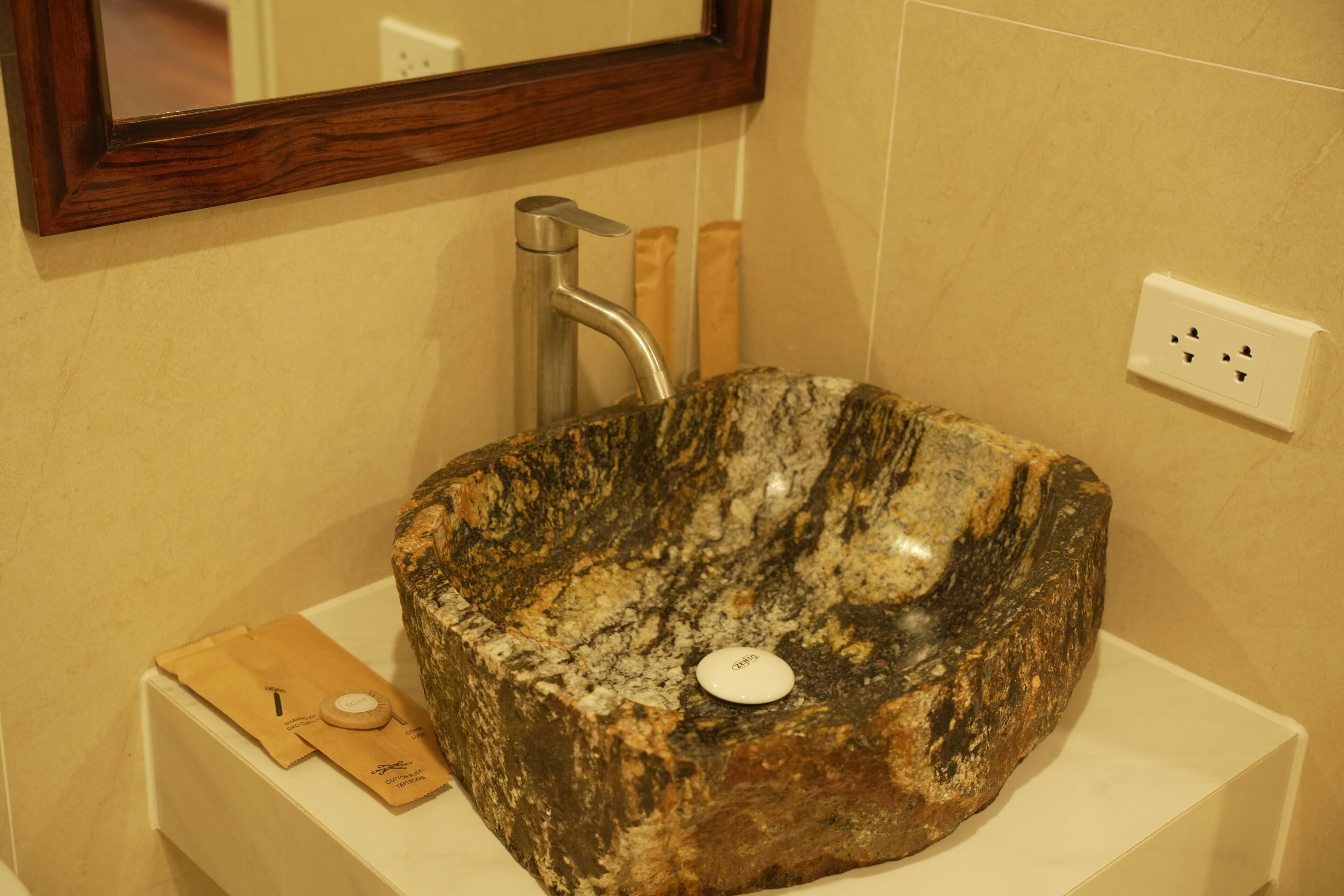 A bathroom with a granite sink, a mirror, and a towel dispenser.