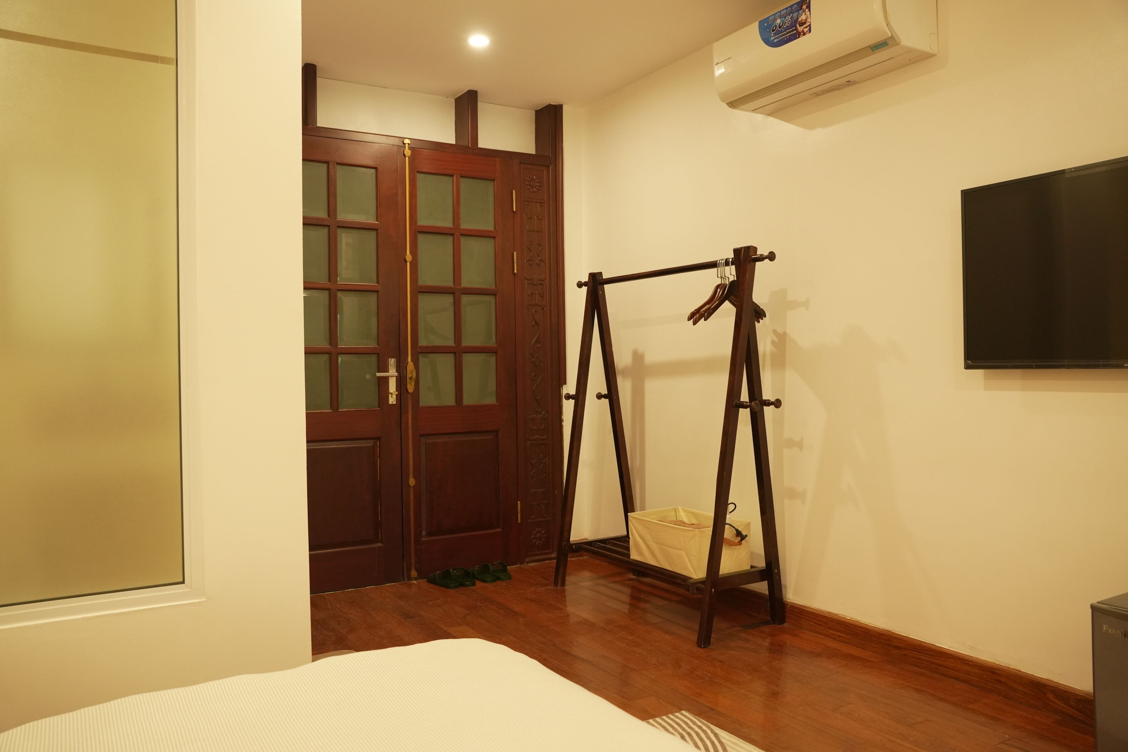 Um quarto com piso de madeira, uma cama, um balanço de madeira, uma porta com painéis de vidro e uma TV fixada na parede.