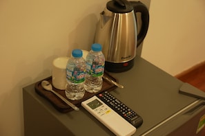 En minibar med fjernbetjening, to vandflasker, en kop og en elkedel.