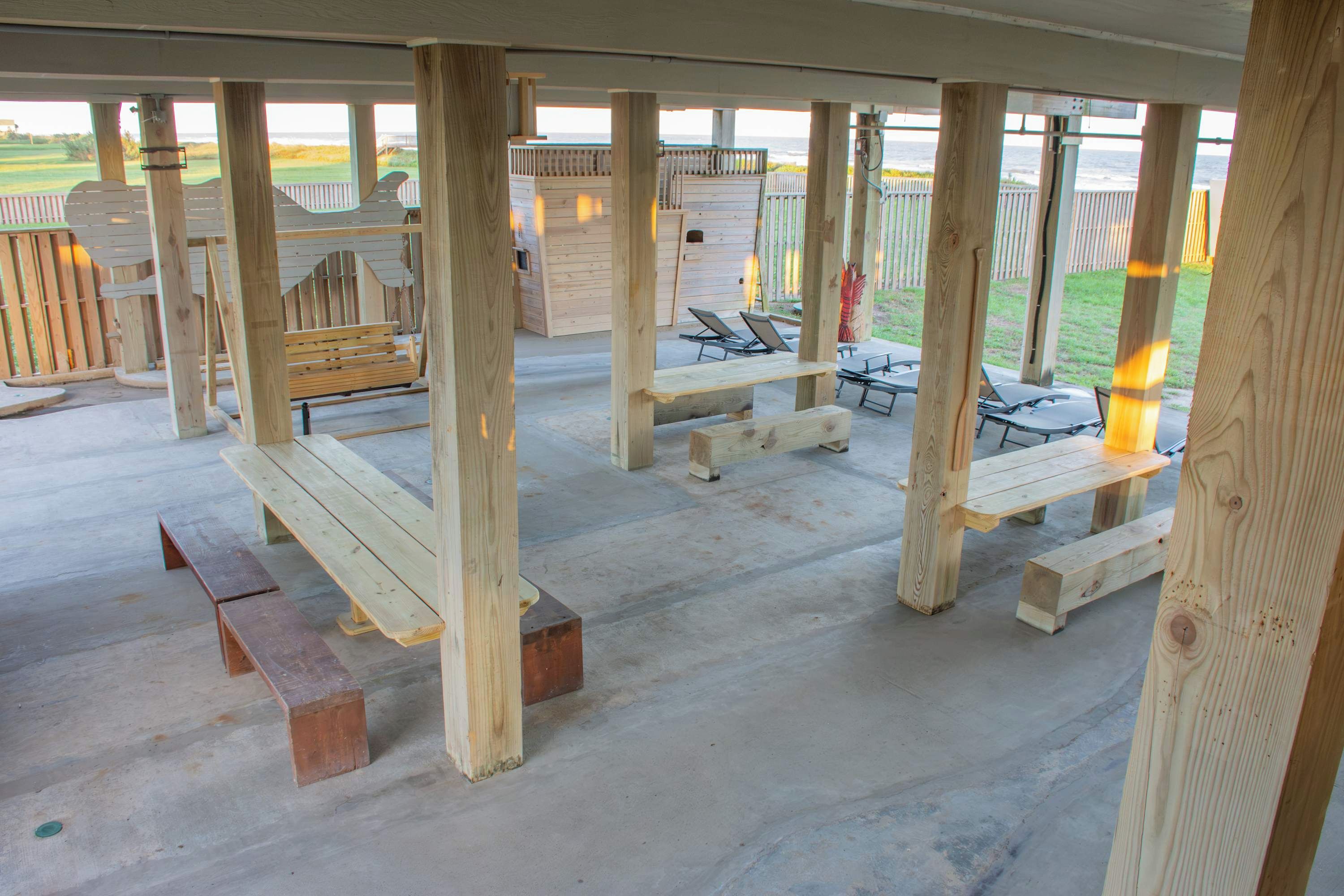 A covered outdoor area with wooden benches and picnic tables, a wooden deck, and a view of the beach.
