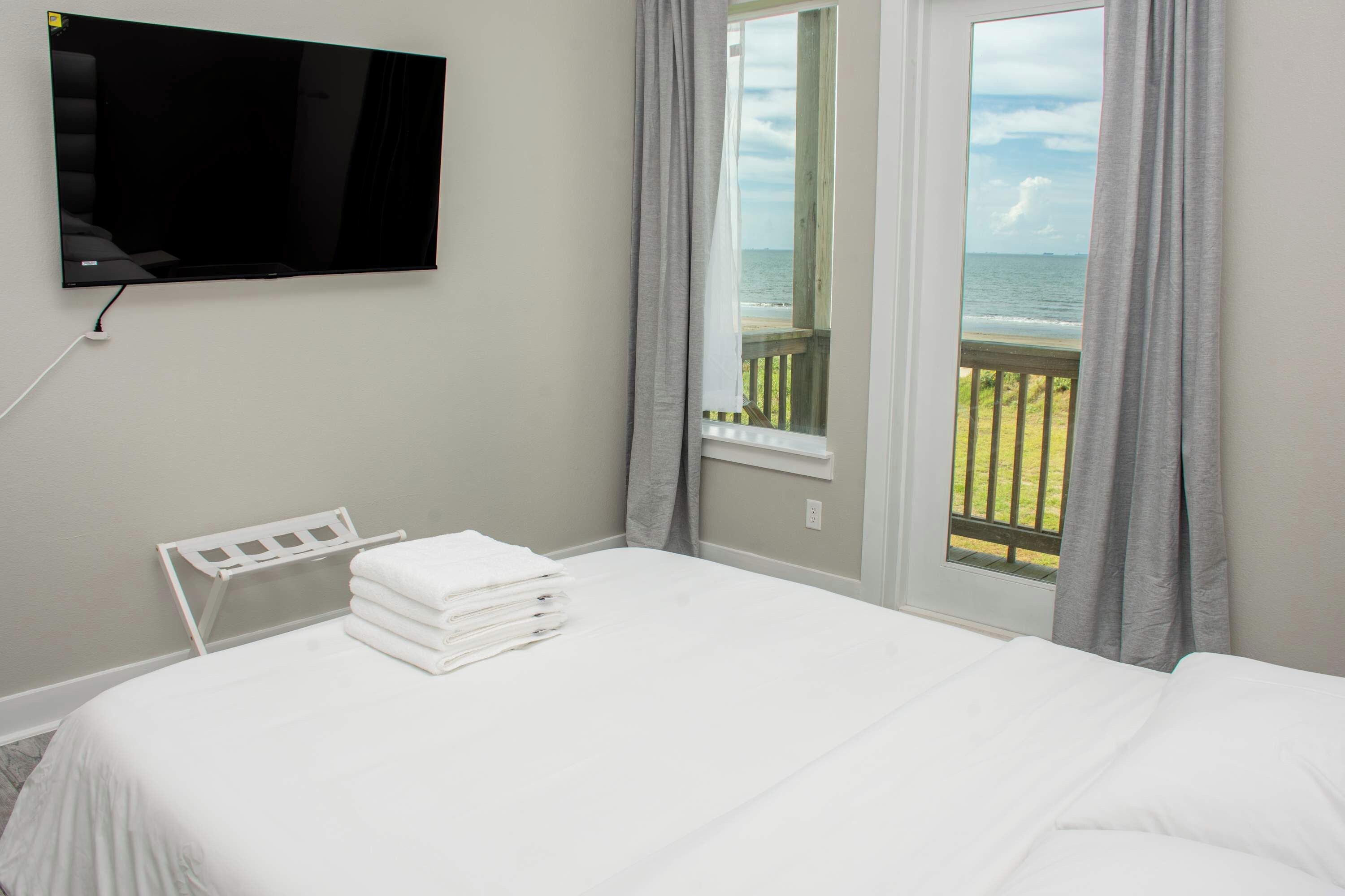 Habitación de hotel con cama, televisor montado en la pared y ventana con vista al océano.
