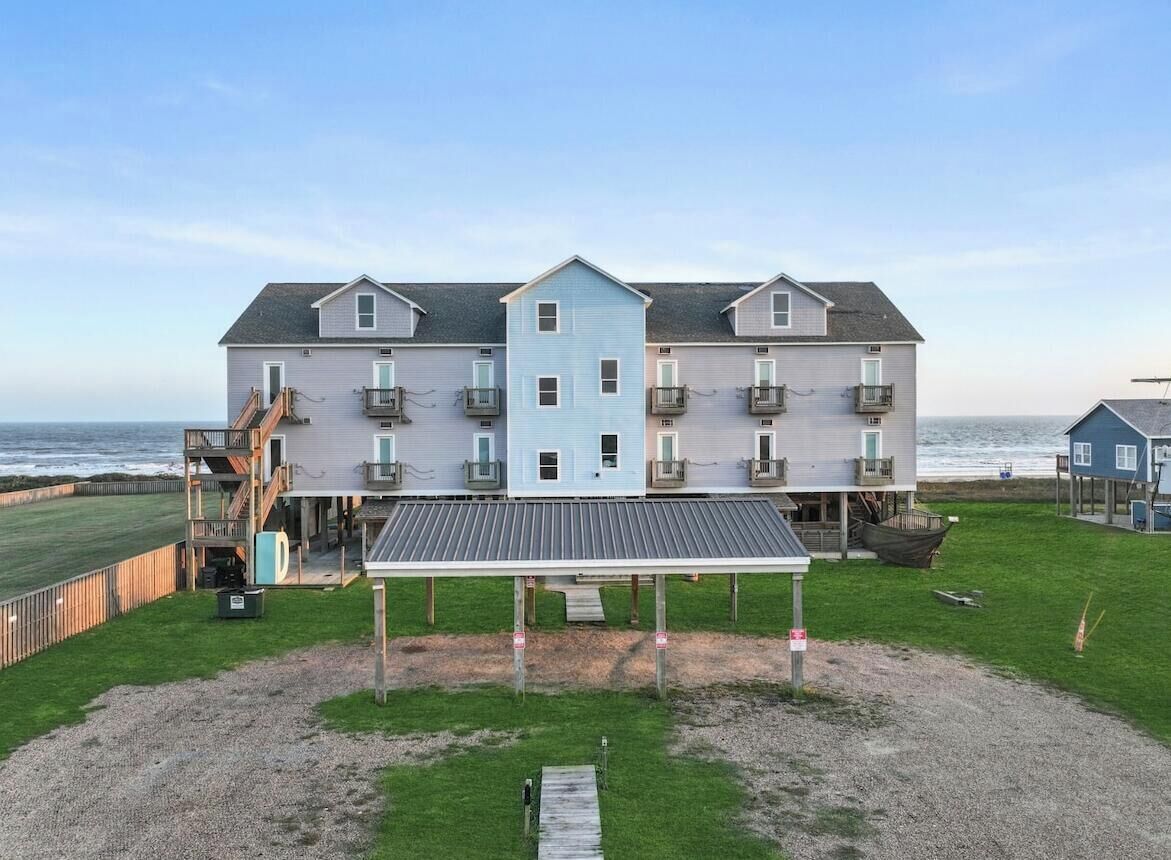 A multi-story building with a covered outdoor area, a staircase leading to the upper floors, and a view of the ocean.