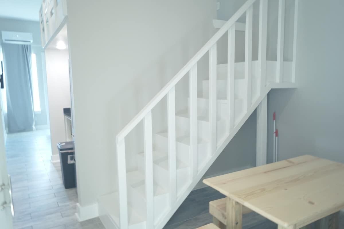 Eine Treppe mit weißer Geländer, ein Holztisch und ein Mülleimer in einem Flur.