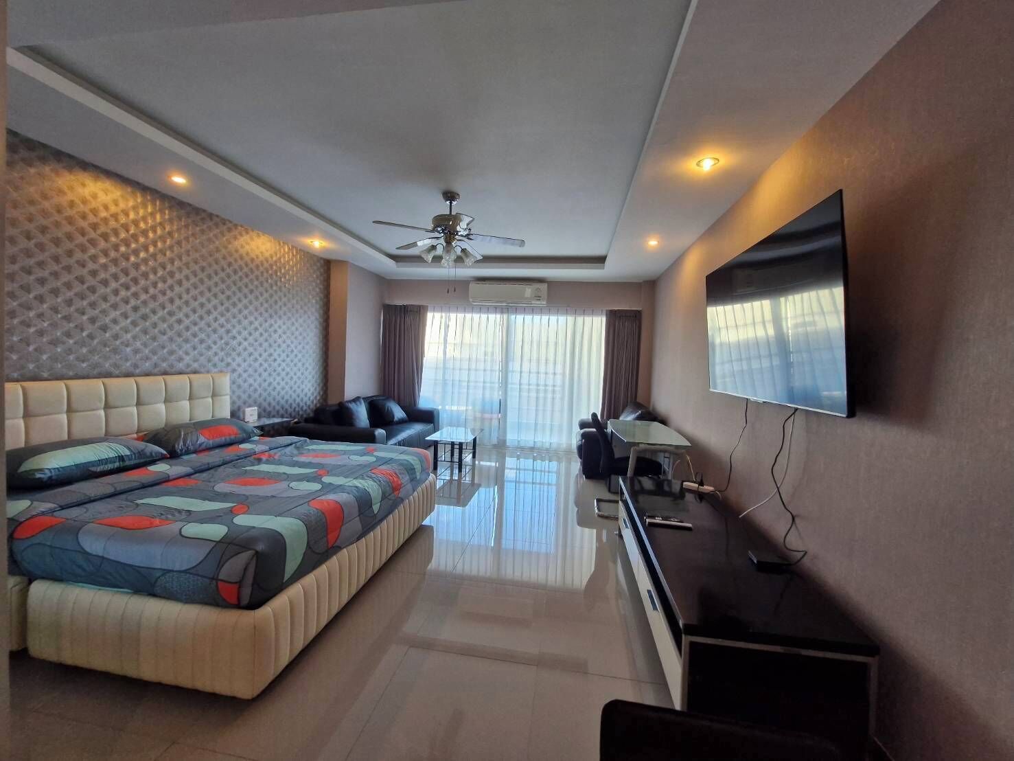 A modern hotel room with a large bed, a sofa, a desk, and a flat-screen TV.
