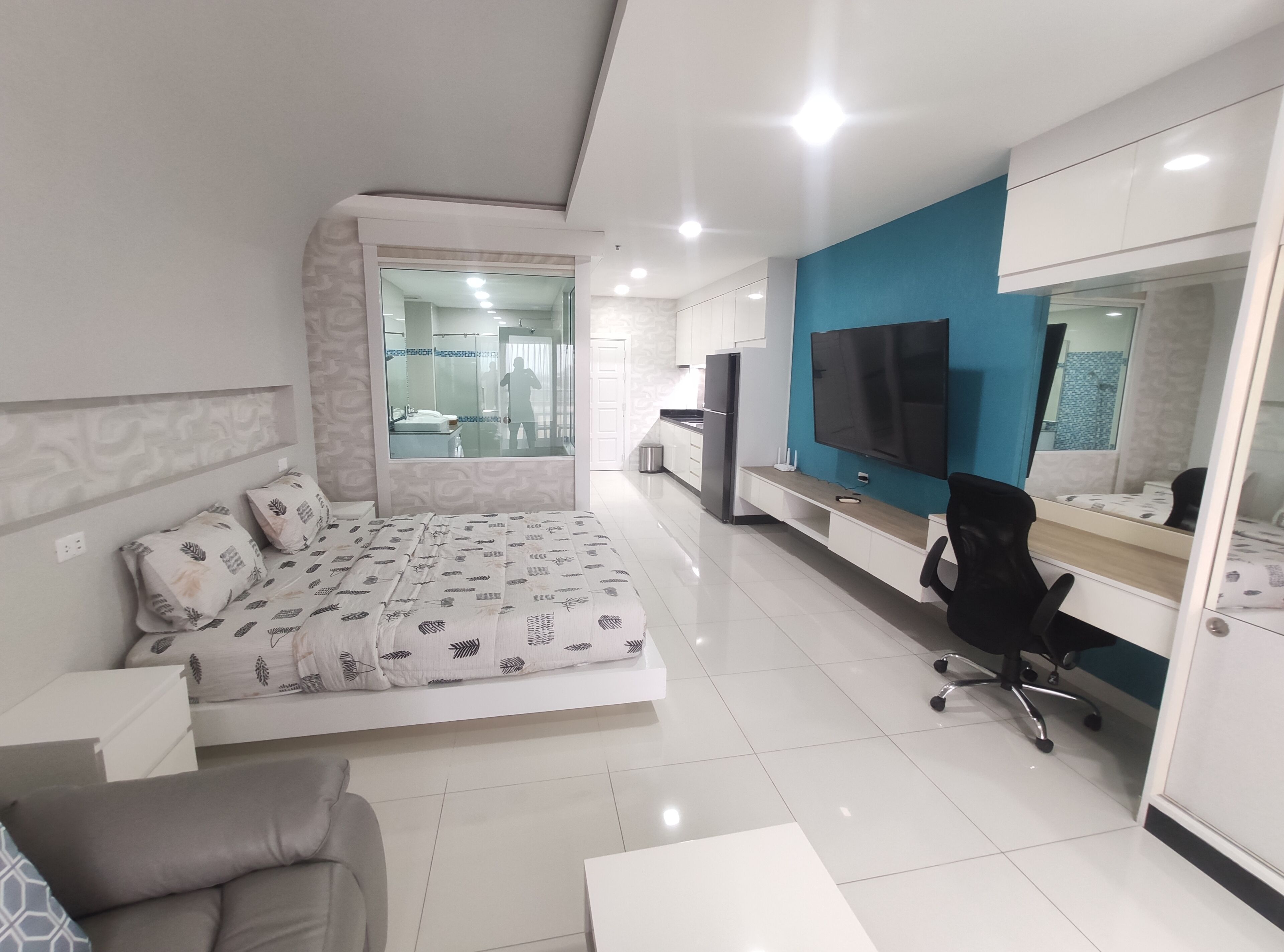 A modern bedroom with a bed, a desk, a chair, and a TV.