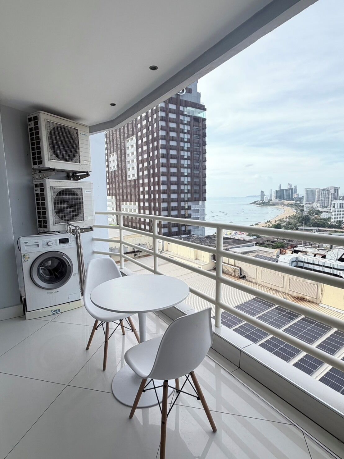 Un balcón con lavadora, mesa y sillas, con vistas a la ciudad y a la playa.