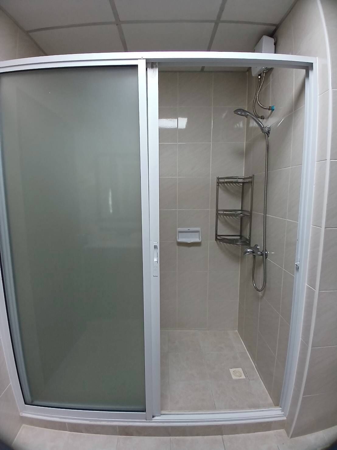 A shower enclosure with a frosted glass door, a handheld showerhead, and a small shelf.
