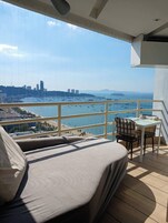 Un balcón con sofá y mesa, con vistas a un puerto deportivo lleno de barcos y un paisaje urbano al fondo.
