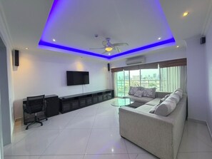 A modern living room with a flat-screen TV, a sofa, a glass coffee table, and a ceiling fan.