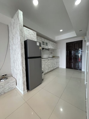 A modern kitchen with a marble backsplash, a black refrigerator, and a tiled floor.