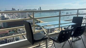 A balcony with a glass table and chairs, overlooking a marina with boats and a cityscape.