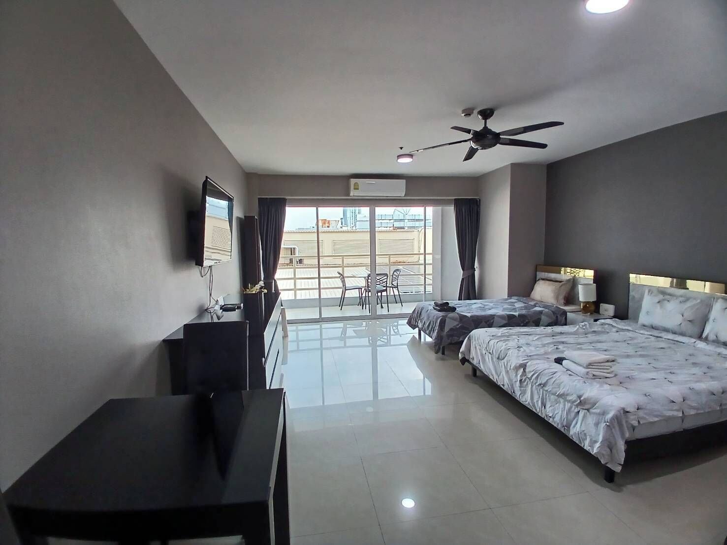 A hotel room with two beds, a desk, a TV, and a balcony with a view.