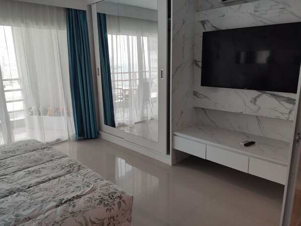 A bedroom with a bed, a TV, a wardrobe, and a balcony with curtains.