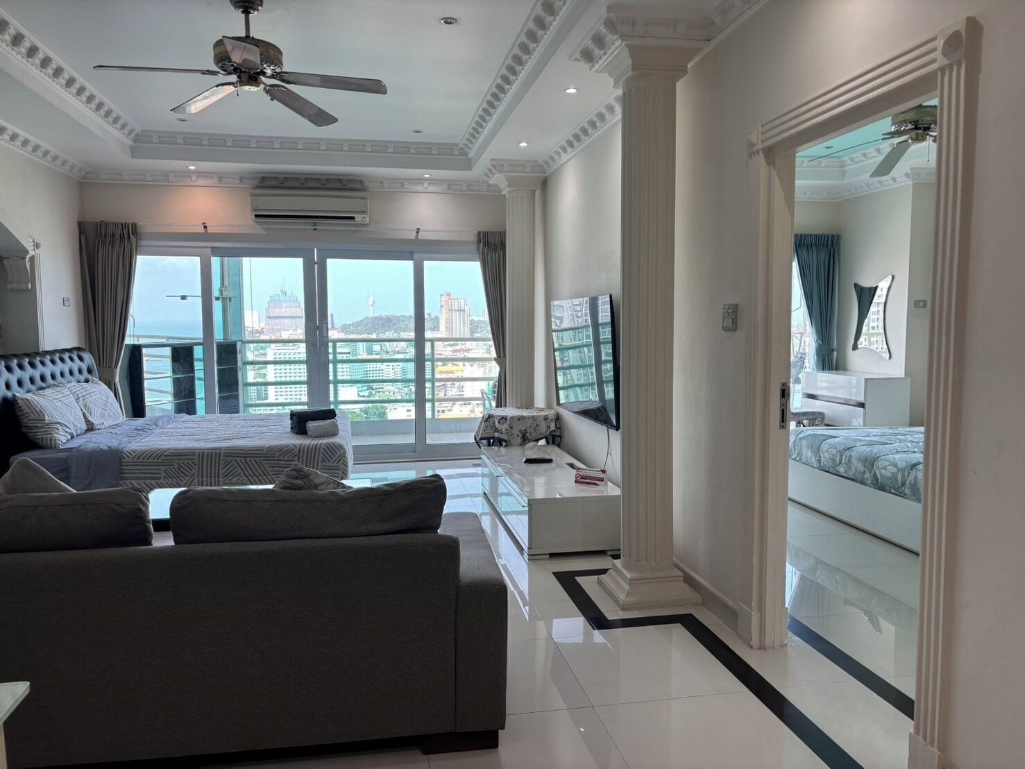A hotel room with a large bed, a sofa, a TV, and a balcony with a city view.