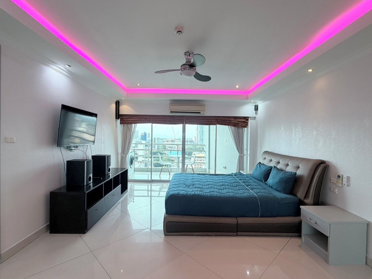 Ein modernes Schlafzimmer mit Bett, Fernseher, Deckenventilator und Blick auf die Stadt.