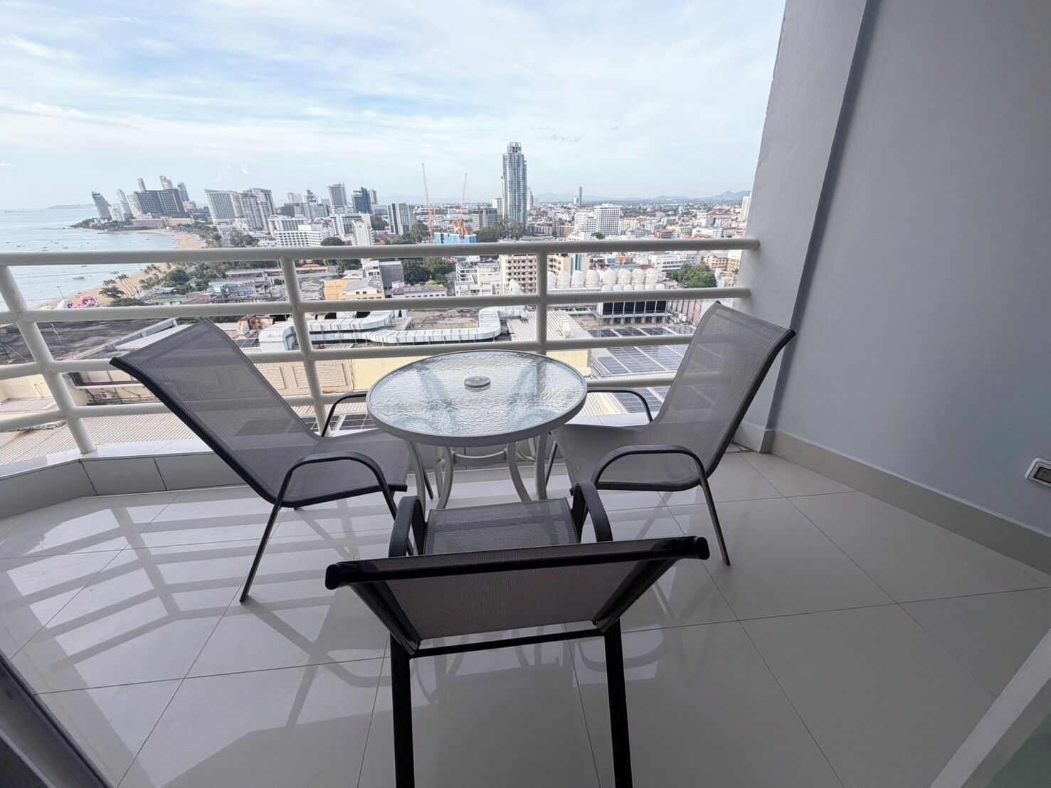 A balcony with a round table and two chairs, overlooking a cityscape with buildings and a beach.