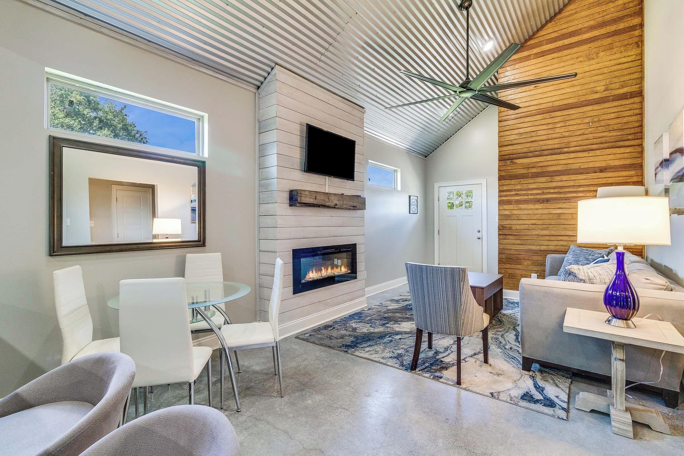 A modern living room with a fireplace, a ceiling fan, and a large window.