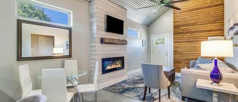 A modern living room with a fireplace, a ceiling fan, and a large window.
