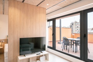 Ein modernes Wohnzimmer mit einem Flachbildfernseher auf einem Holzständer, einer Couch und einem Essbereich mit Stühlen und einem Tisch vor einer großen Glasdoor.