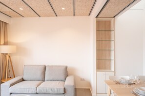 Ein modernes Zimmer mit einer grauen Couch, einer Stehlampe und einem Essbereich mit Tisch für zwei Personen.