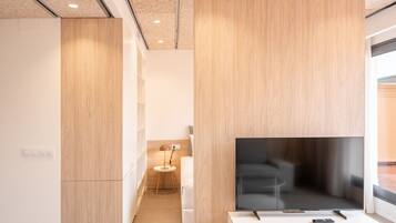 Een moderne hotelkamer met een grote flatscreen-tv, een klein rond tafeltje en een bed met een wit hoofdeinde.