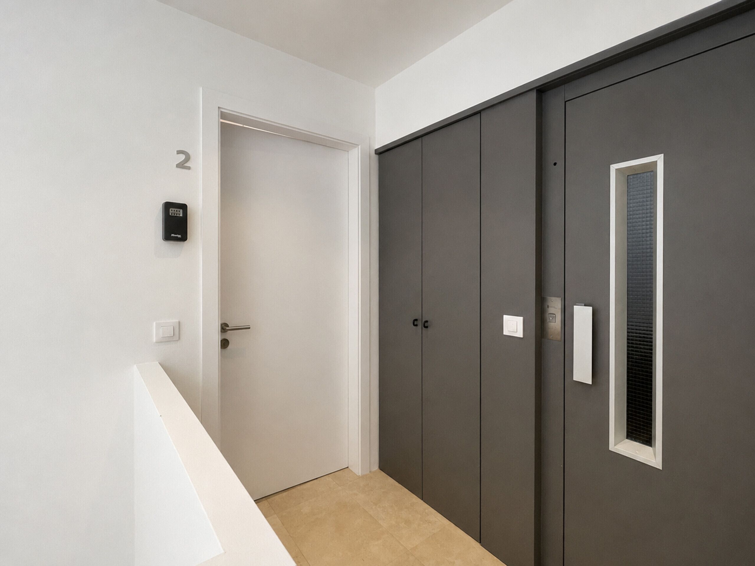 Un pasillo con una puerta, un interfono instalado en la pared y un armario grande con ventana.