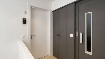 Een gang met een deur, een intercom bevestigd aan de muur, en een grote inloopkast met een raam.