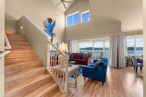 A spacious living area with a wooden staircase, a red sofa, a blue sofa, and a view of the outdoors through large windows. - Club Yakov & 3bdr Lakefront (Hollister)