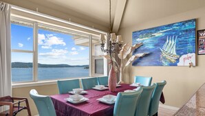 A dining area with a table set for four, a view of the sea through large windows, and a painting on the wall. - Club Yakov & 3bdr Lakefront (Hollister)