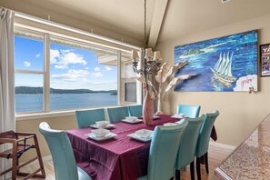 A dining area with a table set for four, a view of the sea through large windows, and a painting on the wall. - Club Yakov & 3bdr Lakefront (Hollister)