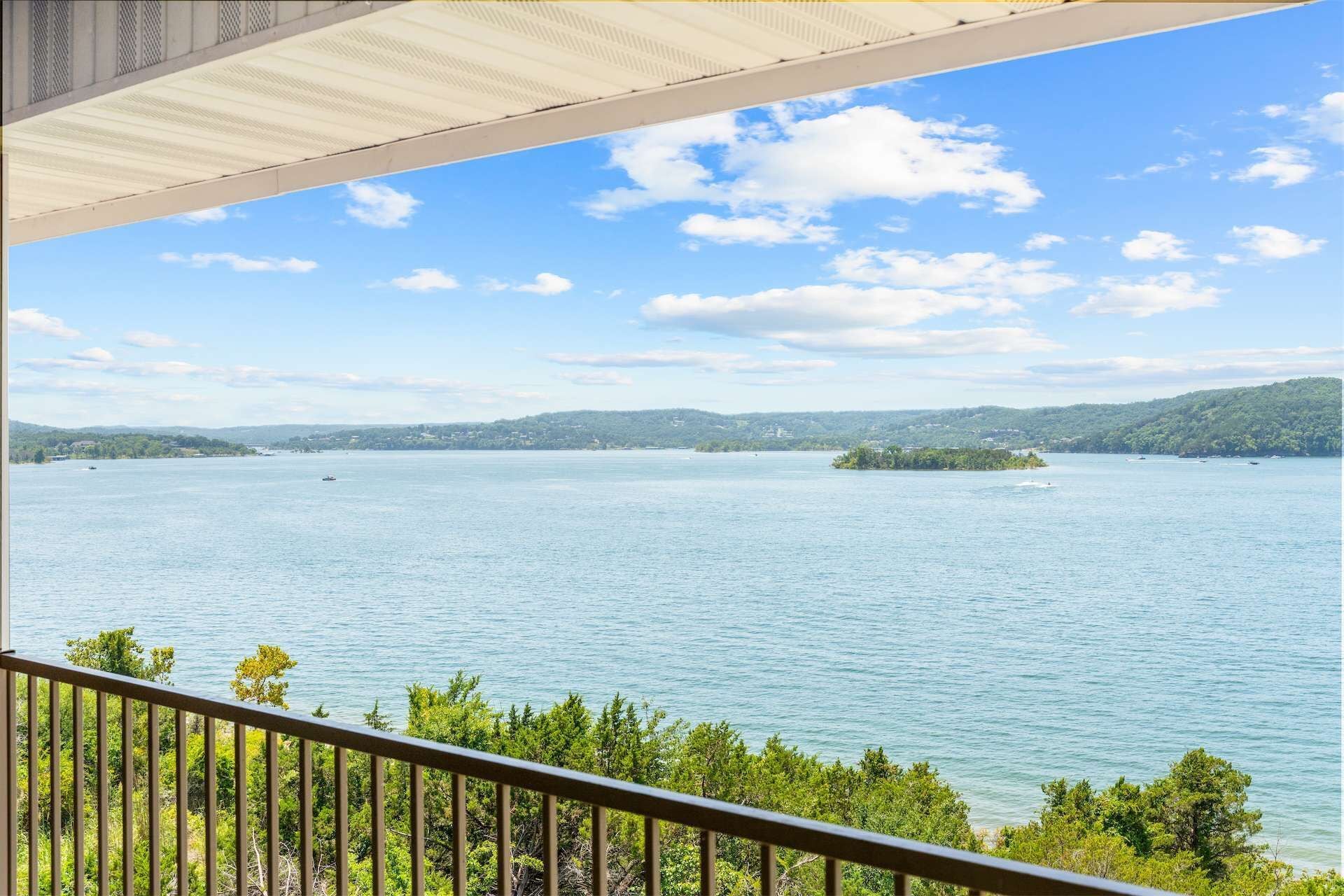 A view of a lake with a small island, a clear sky, and a balcony railing.