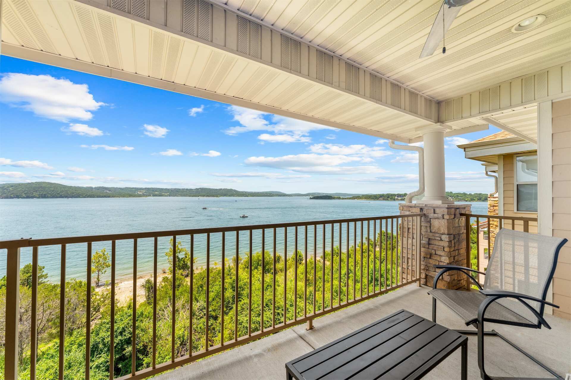 A covered balcony with a view of a lake, a stone pillar, and a bench.