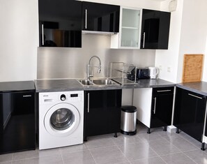 Una cocina moderna con lavadora integrada, lavavajillas y pileta de acero inoxidable.