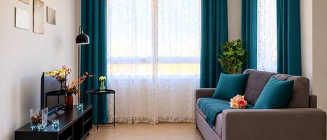 A living room with a sofa, a side table, a lamp, and a window with curtains.
