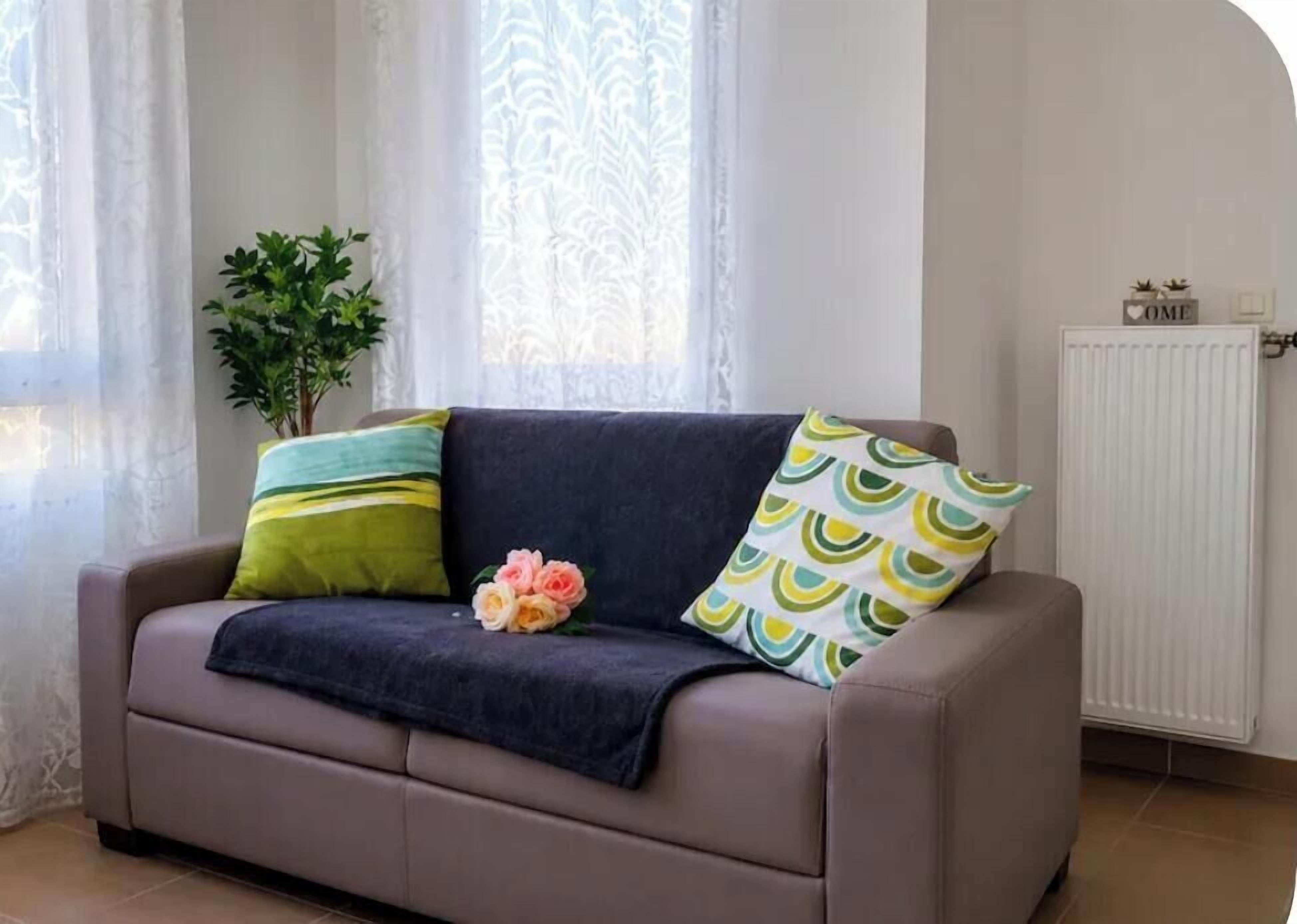 Un canapé recouvert d’un tissu foncé, deux coussins à motifs verts et jaunes, et un bouquet de fleurs.