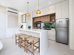 A modern kitchen with a central island, stainless steel refrigerator, pendant lights, and a large window. - Casa Rio | 3BR Enclosed Living & Pool (Kuta Utara)
