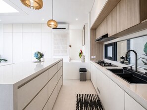 A modern kitchen with white cabinetry, a central island, a black sink, and pendant lighting. - Casa Rio | 3BR Enclosed Living & Pool (Kuta Utara)