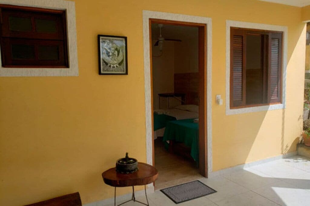 Um quarto com uma cama, uma mesinha com abajur e uma porta que dá para outro cômodo.