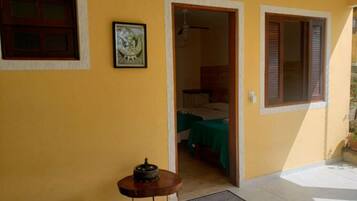 Um quarto com uma cama, uma mesinha com abajur e uma porta que dá para outro cômodo.