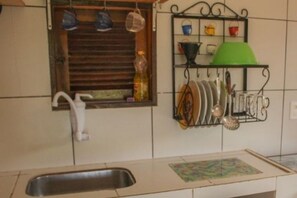Une cuisine équipée d’un évier, d’une fenêtre avec des stores et d’un porte-ustensiles.