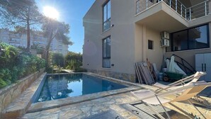 Un bâtiment moderne à deux étages doté d’une piscine, de revêtements de sol en pierre et de mobilier d’extérieur.
