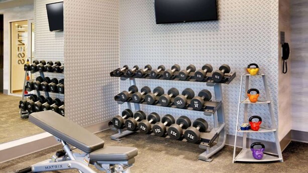 Een sportschool met gewichthefapparatuur, waaronder dumbbells en kettlebells, en een bank.
