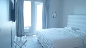 Un dormitorio con cama, una silla, un espejo y una ventana con cortinas.