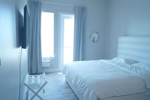 Ein Schlafzimmer mit einem Bett, einem Sessel, einem Spiegel und einem Fenster mit Vorhängen.