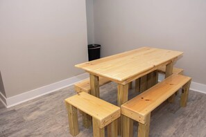 A wooden table with four benches in a room with grey walls and a grey floor. - Casa Dora Summer Waves (Bolivar Peninsula)