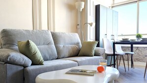 A modern living room with a grey sofa, white coffee table, and a dining area with a table and chairs. - PINTOR SOROLLA elegant apartment (Benidorm)
