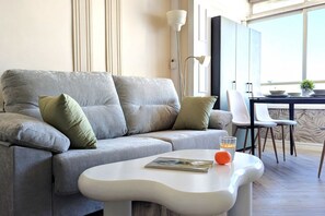 A modern living room with a grey sofa, white coffee table, and a dining area with a table and chairs. - PINTOR SOROLLA elegant apartment (Benidorm)