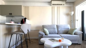 A modern living space with a kitchen area, a grey sofa, a white coffee table, and a bar stool. - PINTOR SOROLLA elegant apartment (Benidorm)